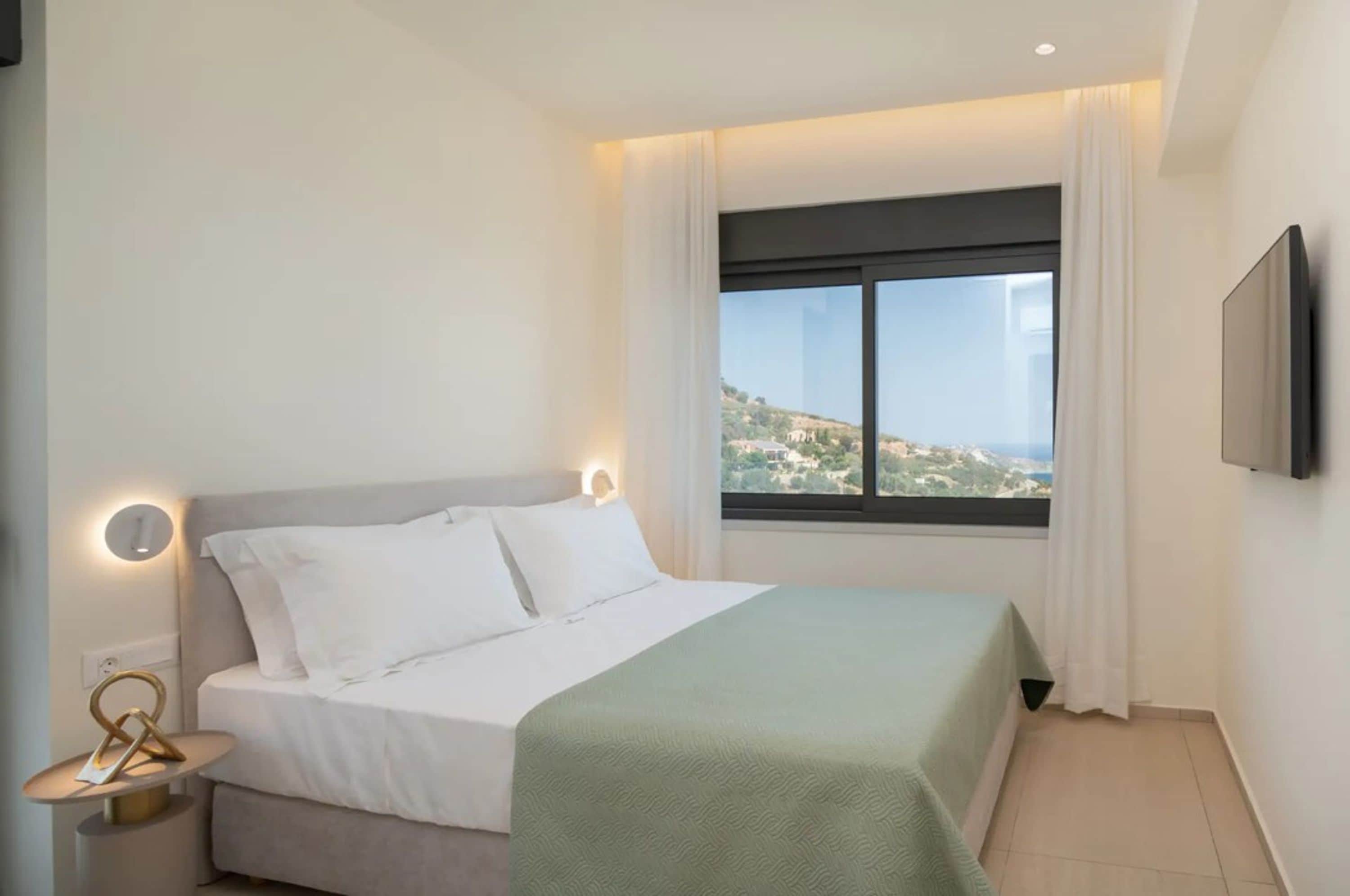 A hotel room with a bed, a nightstand, a TV, and a window with a view of a landscape.