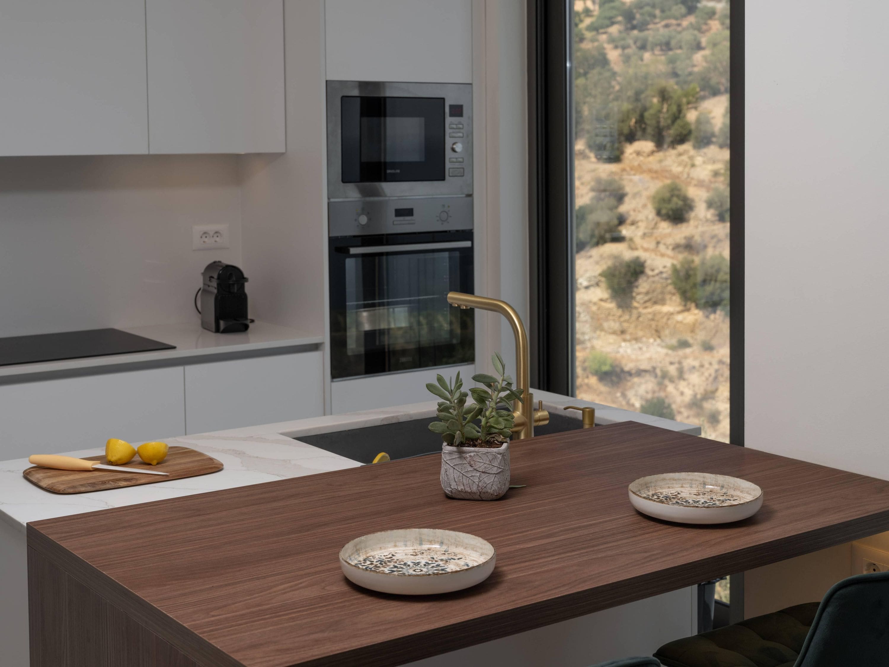 Una cocina moderna con horno empotrado, microondas y un amplio ventanal con vistas a un paisaje montañoso.