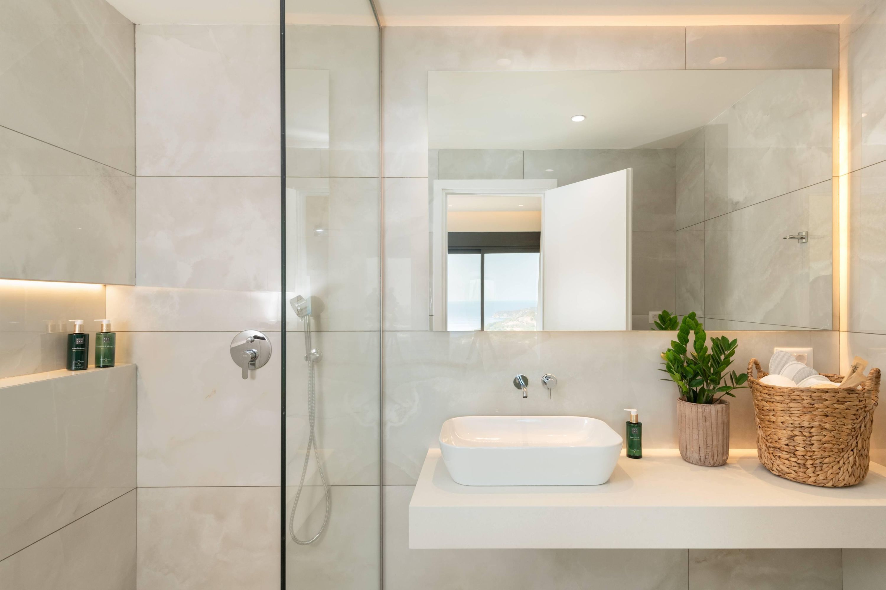 A modern bathroom with a glass-enclosed shower, a white sink, and a mirror above it.