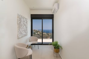 A balcony with a view of the sea, a chair, a small table, and a potted plant.