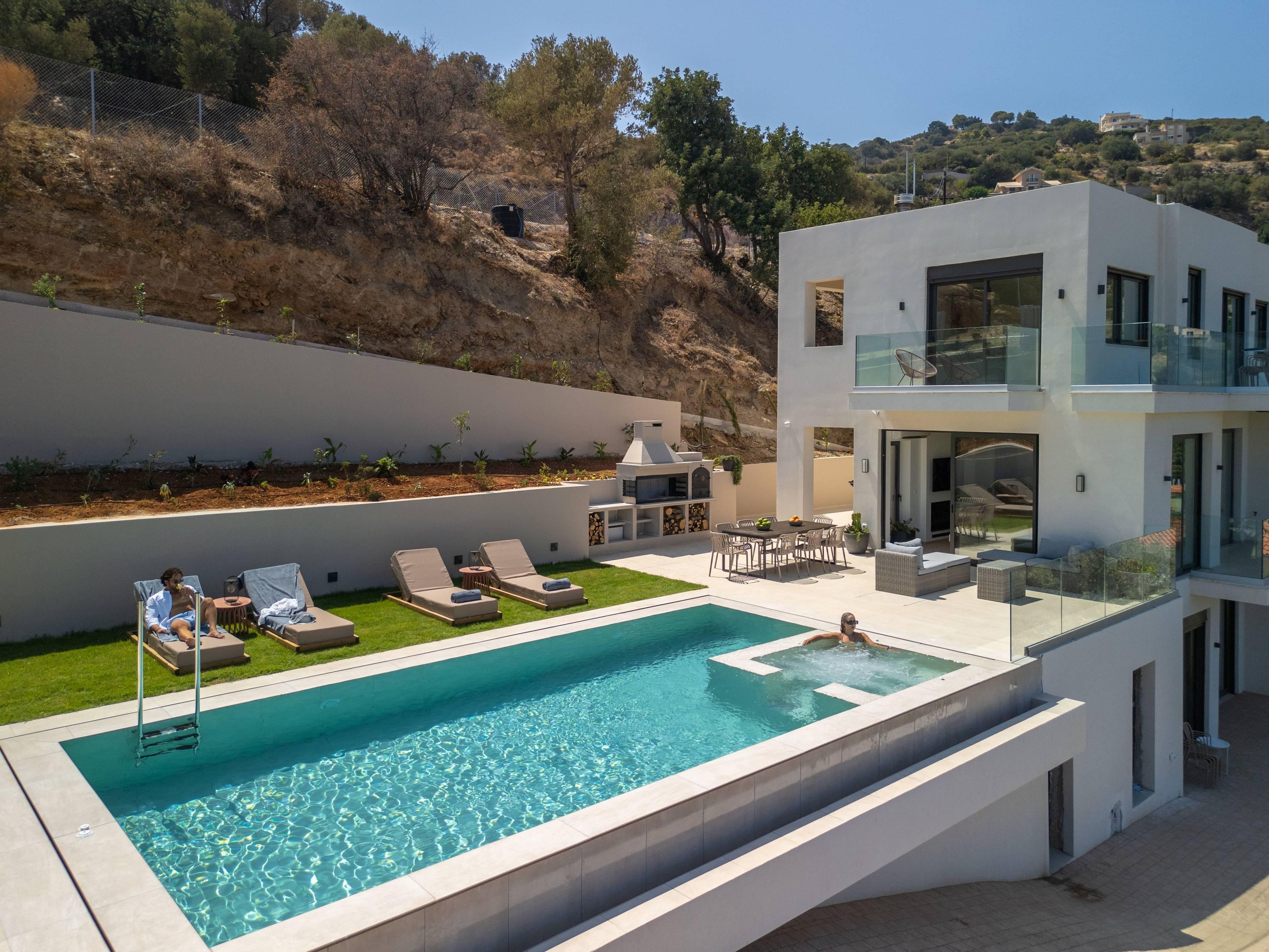 A modern outdoor pool area with lounge chairs, a barbecue, and a dining set.