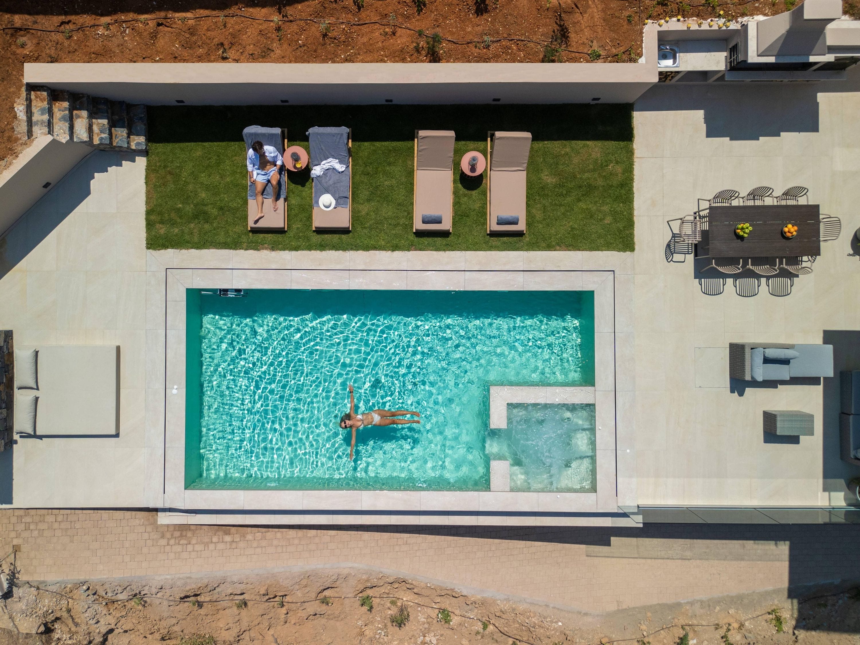 Vista aérea de un moderno espacio de piscina con sillas de descanso, una mesa de comedor y una alberca.