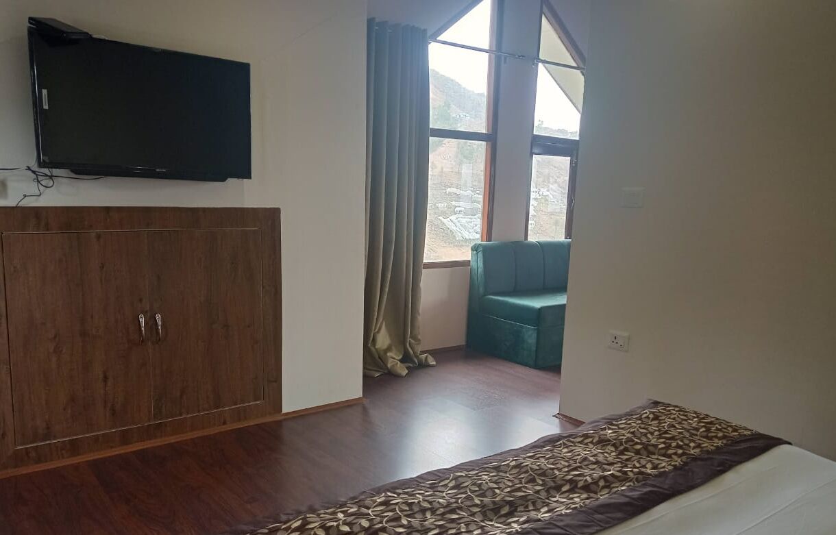 A room with a bed, a wardrobe, a television, and a window with curtains.