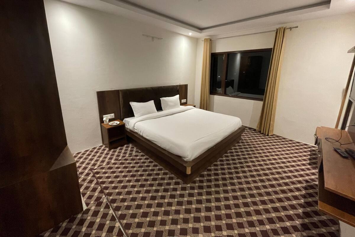 Una habitación de hotel con una cama grande, una mesita de noche, un escritorio y una ventana con cortinas.