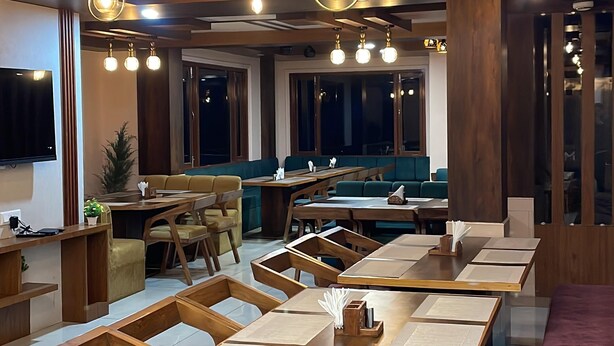 A modern dining area with wooden tables and chairs, a central bar area, and large windows providing natural light. - Hotel Apple View Narkanda (Theog)
