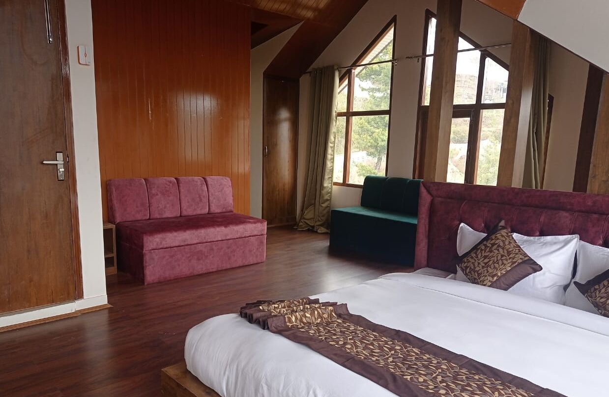 A bedroom with a large bed, a wooden wardrobe, a red sofa, and a green sofa.