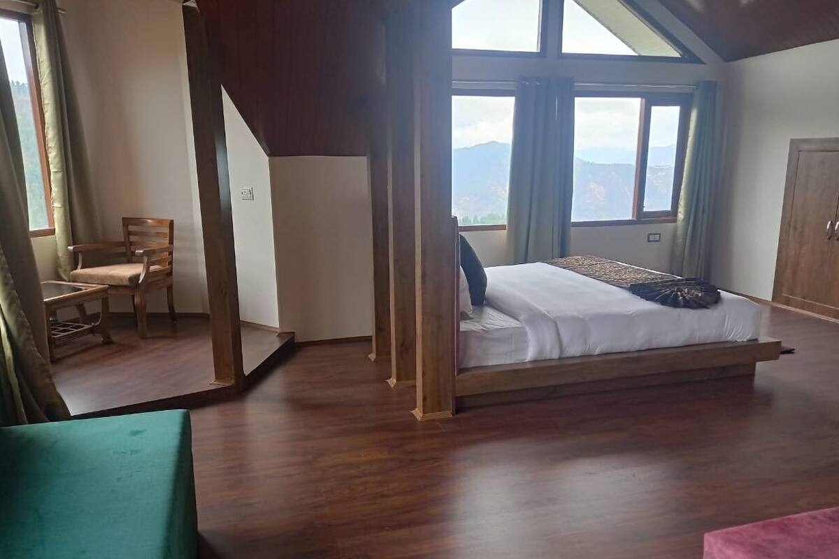 Un dormitorio con una cama grande, suelo de madera, una silla y vistas a montañas a través de una ventana.