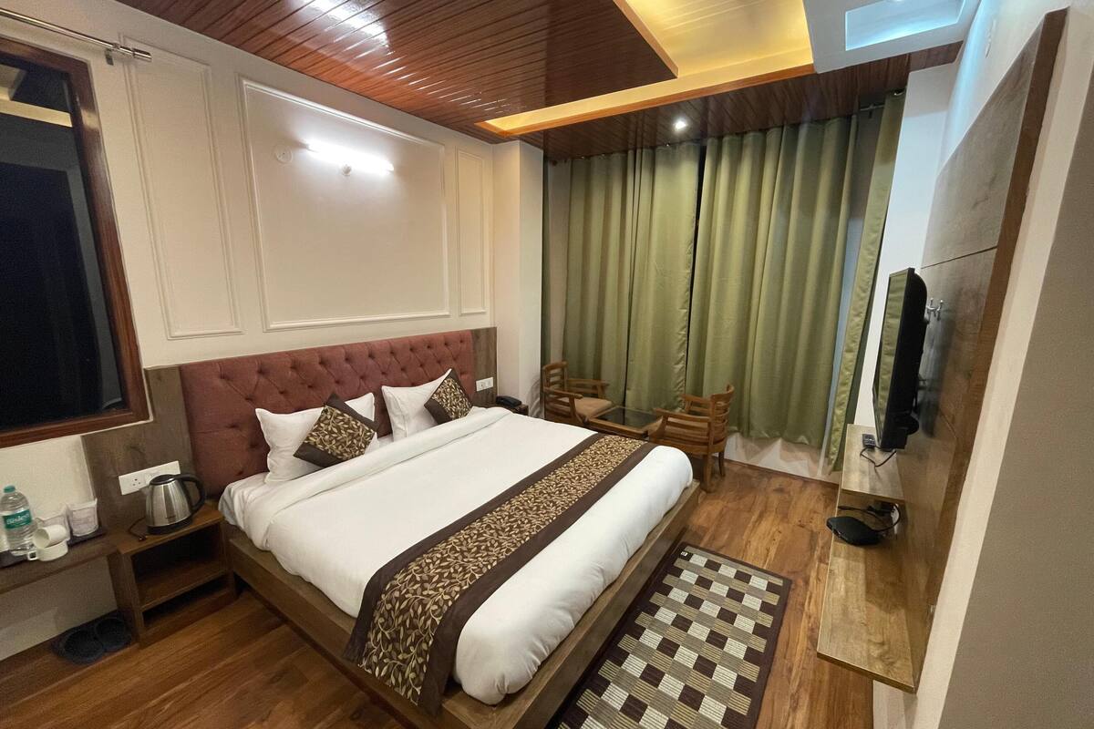 Habitación de hotel con una cama grande, piso de madera, televisor, escritorio y ventana con cortinas.
