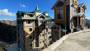 A multi-story hotel with a green roof and a sign that reads "HOTEL". - Hotel Apple View Narkanda (Theog)
