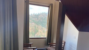 A room with a large window, wooden furniture, and a view of a hilly landscape. - Hotel Apple View Narkanda (Theog)