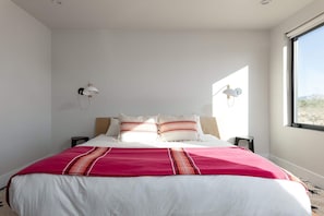 A bedroom with a bed, two bedside lamps, a window, and a view of the outside.