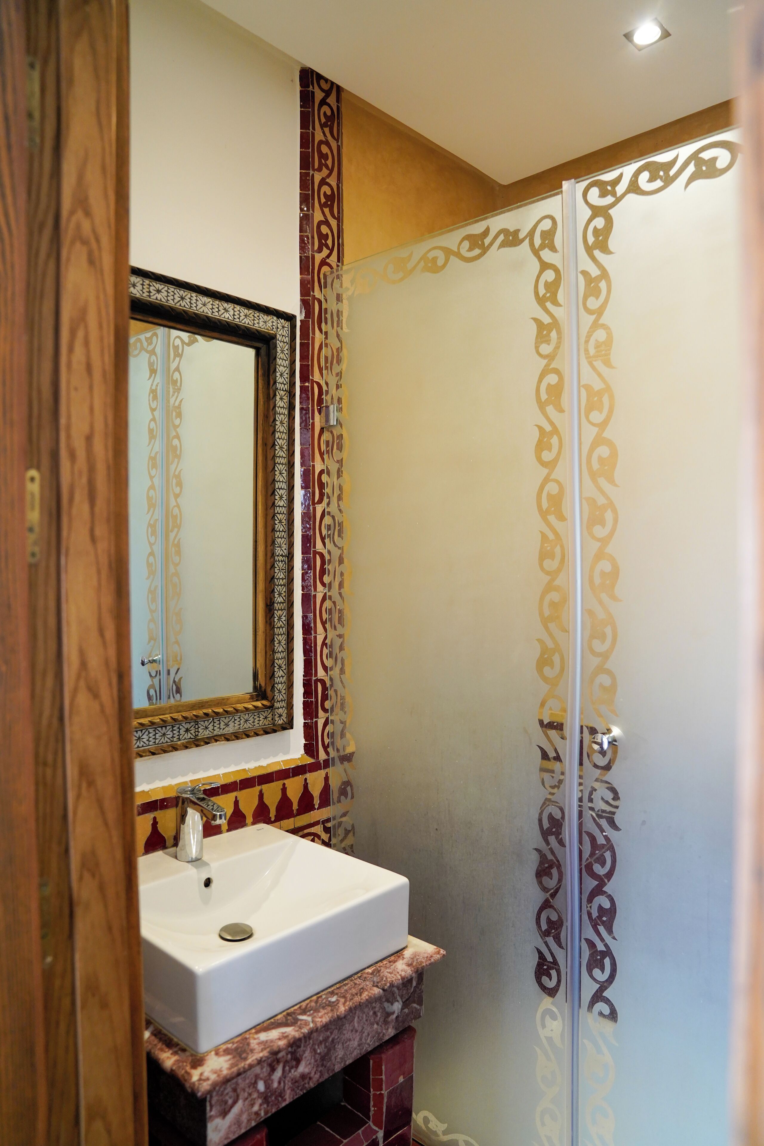 A bathroom with a marble sink, a mirror with an ornate frame, and a shower with decorative panels.