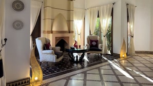 A spacious room with a fireplace, two armchairs, a round table, and patterned flooring. - Palais Volteras (Marrakech)