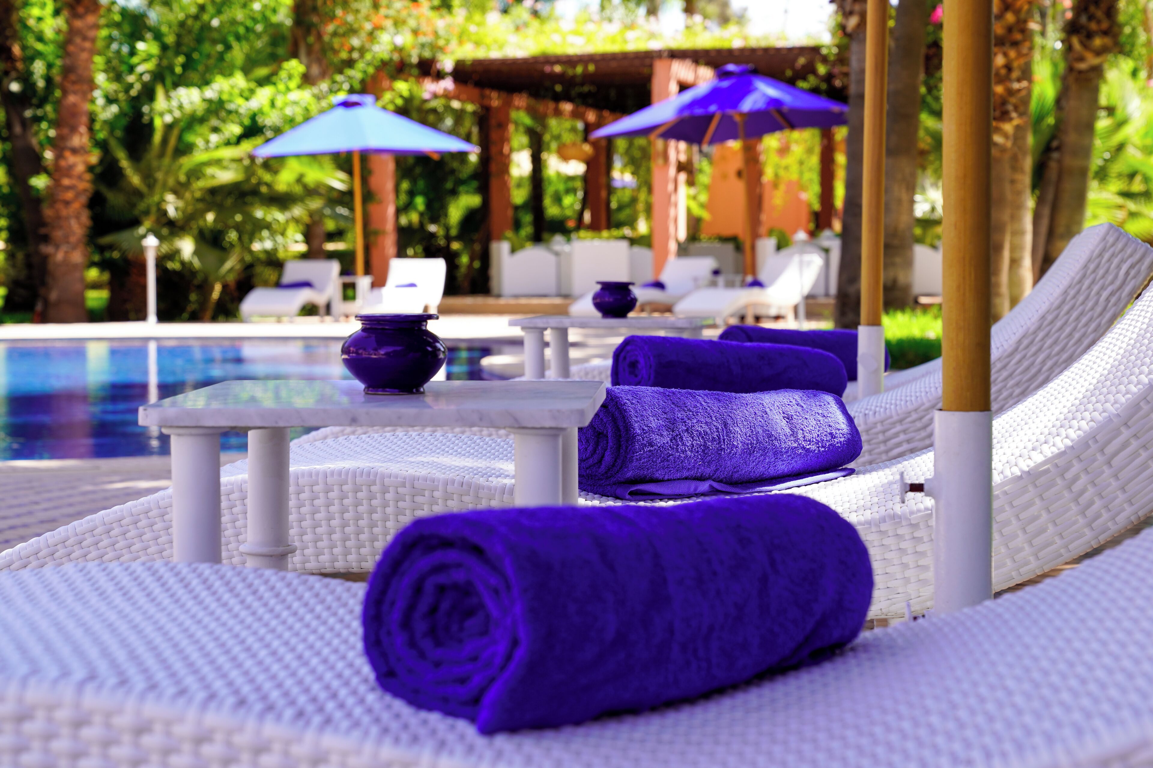 A poolside area with white lounge chairs, purple towels, and blue umbrellas.