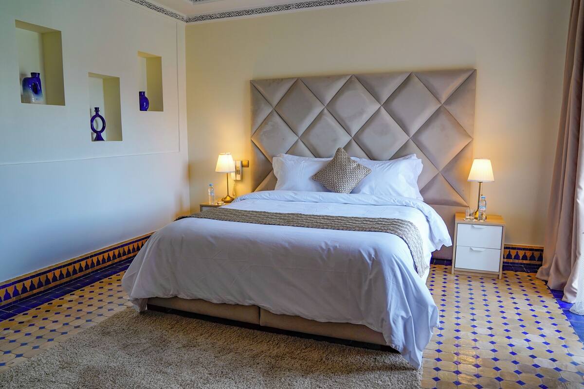 A neatly arranged bedroom with a large bed, two bedside tables with lamps, and a patterned floor.