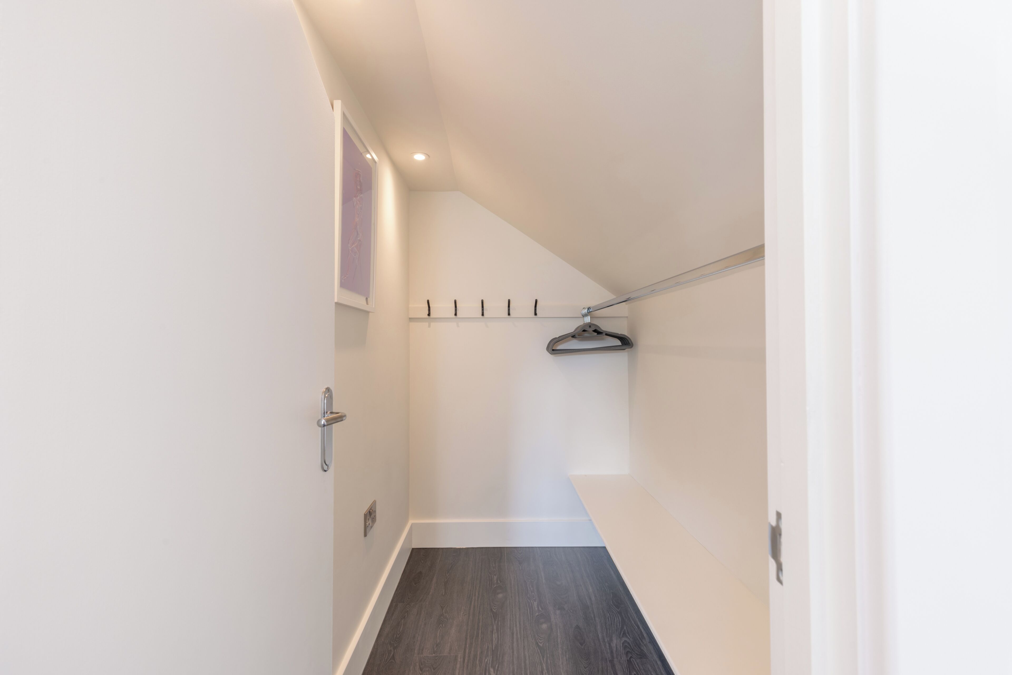 A narrow hallway with a wooden floor, a coat rack, and a door on the left.