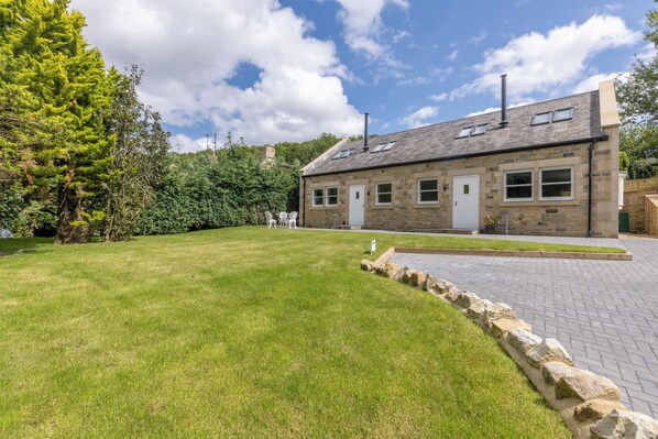 A stone house with a grassy yard and a paved driveway. - Babbling Burn - North East Escapes (Belford)