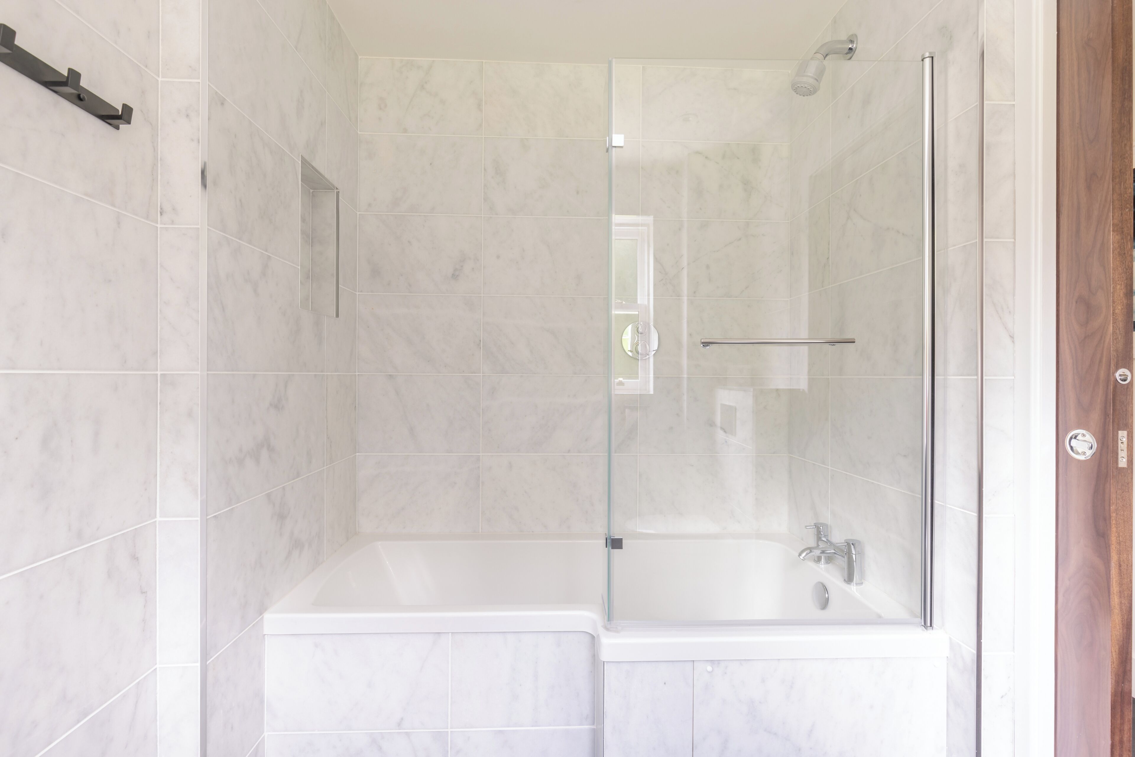 A modern bathroom with a glass-enclosed shower, a separate bathtub, and a marble-tiled wall.