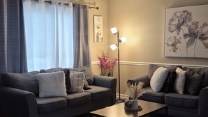 En stue med to sofaer, et sofabord, en gulvlampe og et blomsterbillede på væggen.