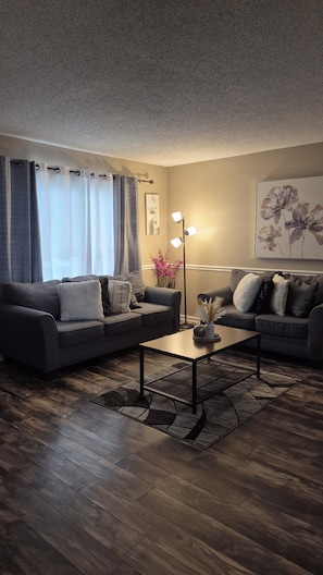 Un salon avec deux canapés, une table basse, un lampadaire et un tableau représentant des fleurs accroché au mur.