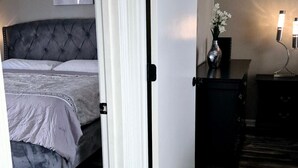 Ein Schlafzimmer mit Bett, Nachttisch, Kommode und einer Tür zu einem weiteren Raum.