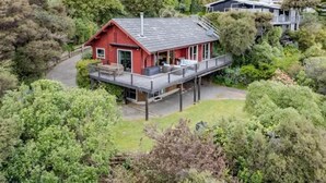 A red house with a balcony, surrounded by greenery and hills.