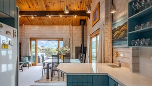 A modern kitchen with a central island, wooden ceiling, and a view of the outdoors.