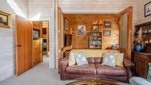 A cozy living room with a leather sofa, a glass coffee table, wooden walls, and a bookshelf.