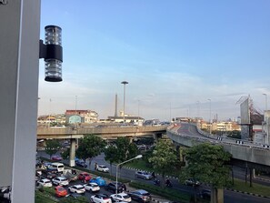 A view of a busy urban street with multiple lanes of traffic, a bridge, and a large building with a distinctive tower. - Ther Bangkoknoi Hotel (Bangkok)