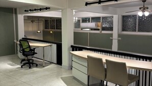 Een moderne kantoorruimte met een lang bureau, meerdere stoelen, een radiator en een plafondlamp.