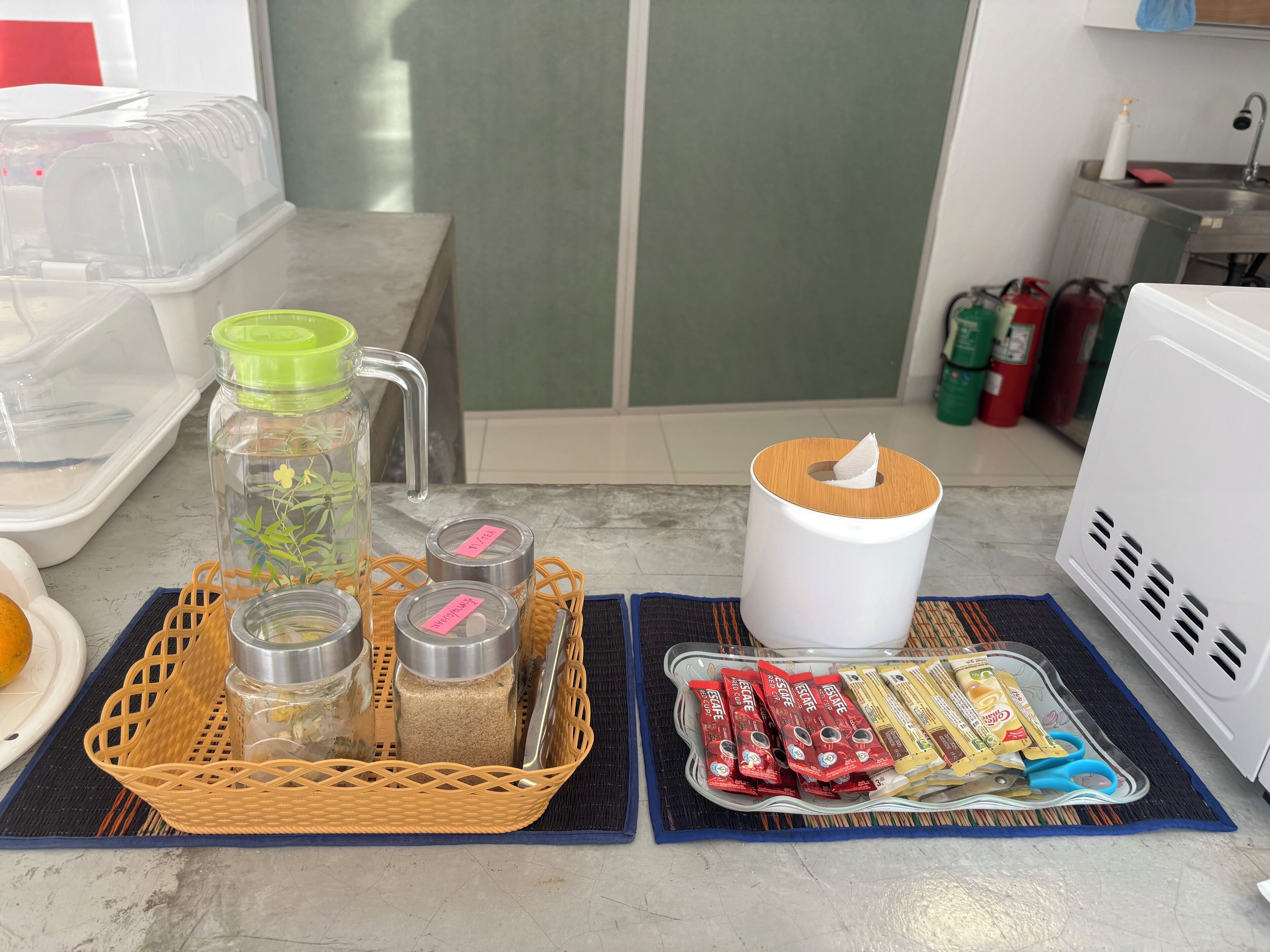 Eine Küchenarbeitsplatte mit verschiedenen Gegenständen, darunter eine Wasserkanne, Gewürzbehälter, eine Papiertuchrolle und verpackte Snacks.