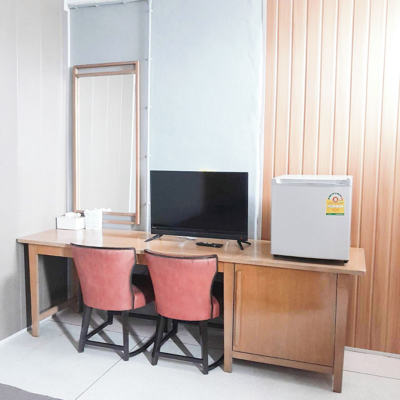 A small room with a wooden desk, two pink chairs, a black TV, and a white refrigerator.