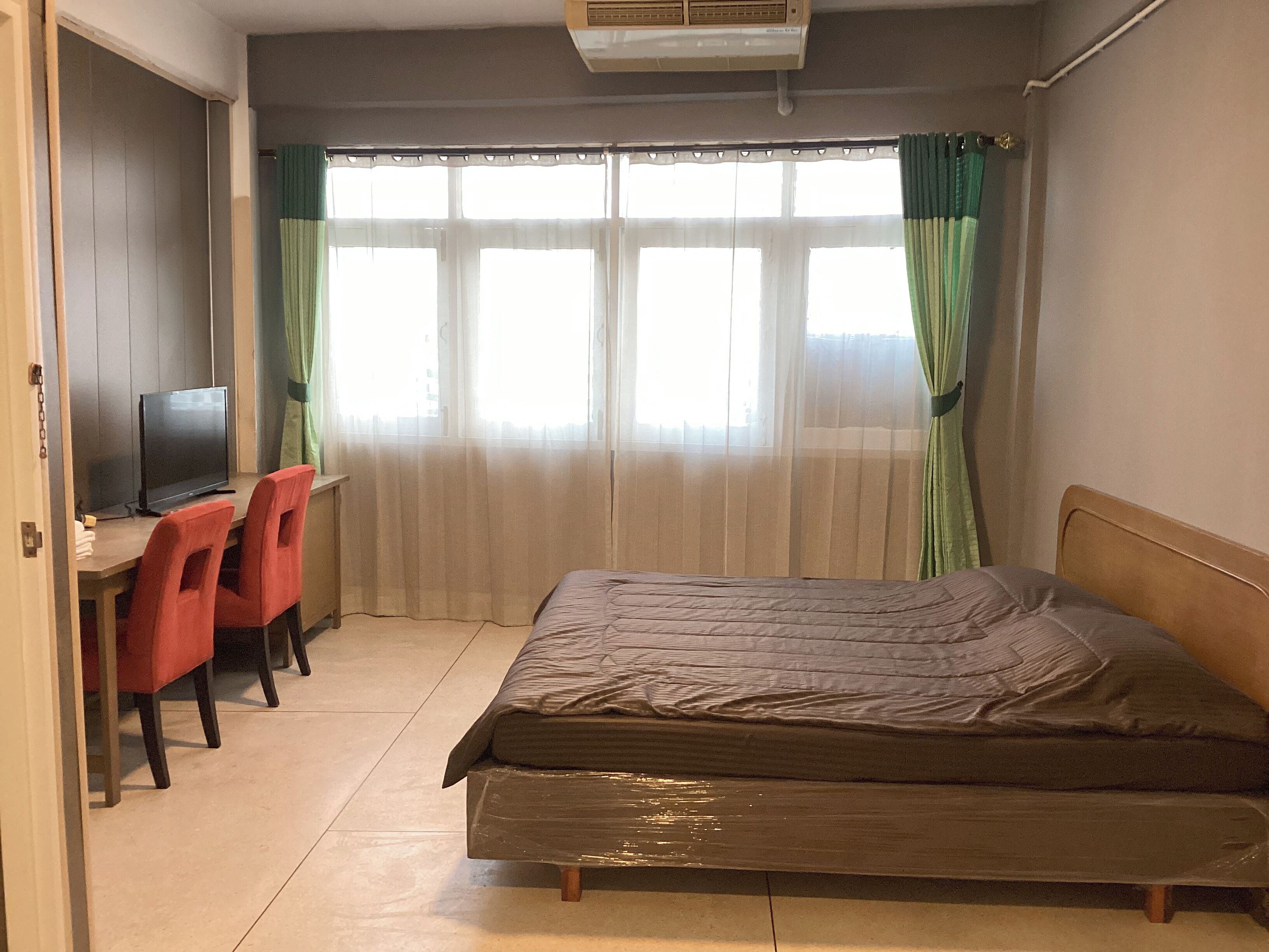 A room with a bed, a desk with a television, and a window with curtains.
