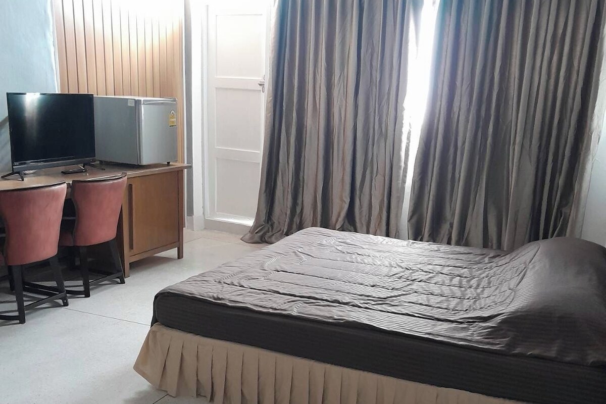 Um quarto com uma cama, uma escrivaninha com um computador e uma televisão.