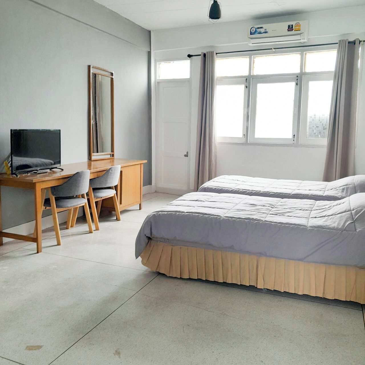 Quarto com cama, escrivaninha, cadeira, televisão e janela com cortinas.