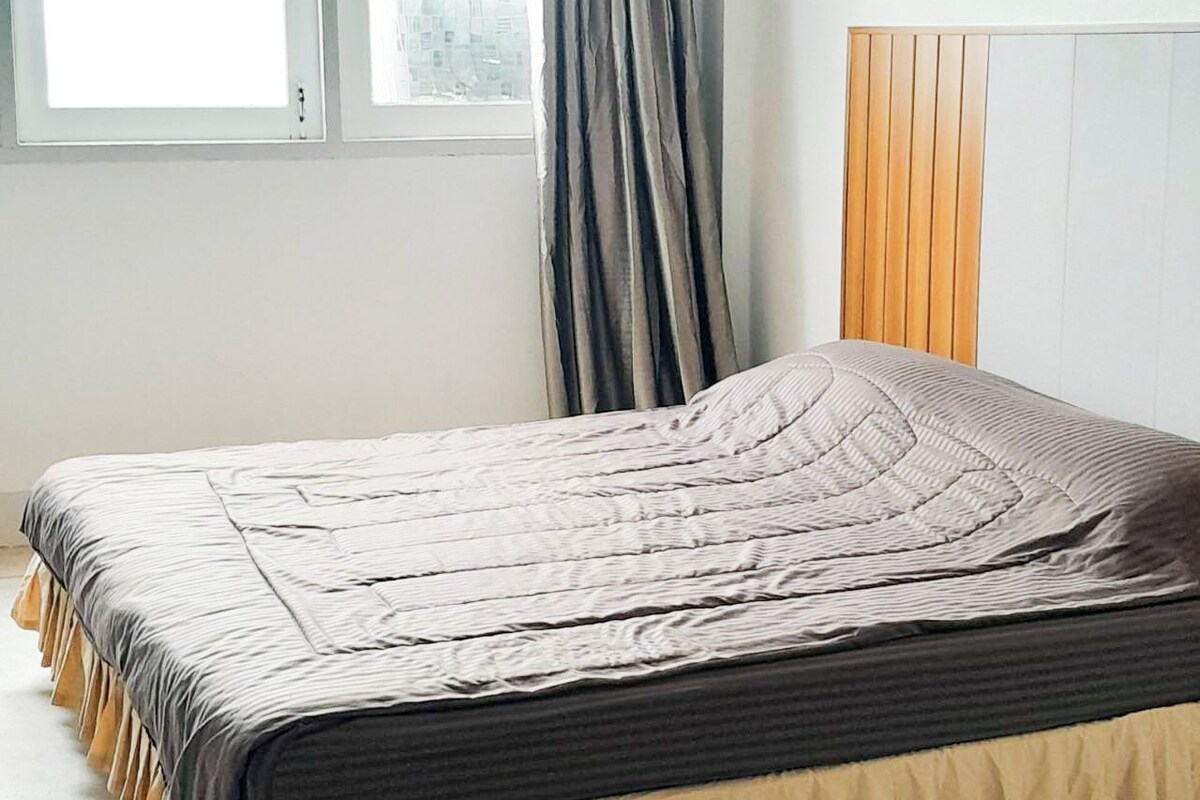 Un lit avec une couvre-lit à rayures beiges et grises, une tête de lit en bois et une fenêtre avec des rideaux.