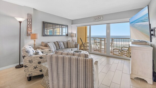 A spacious living room with a large window overlooking a balcony, a sofa set, and a small table.