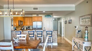 A kitchen with wooden cabinets, a stainless steel refrigerator, a dining table with chairs, and a 'Welcome!' sign.