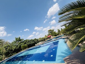 A swimming pool with clear blue water, surrounded by lush greenery and a clear sky. - deora resort and hotel (Jodhpur)