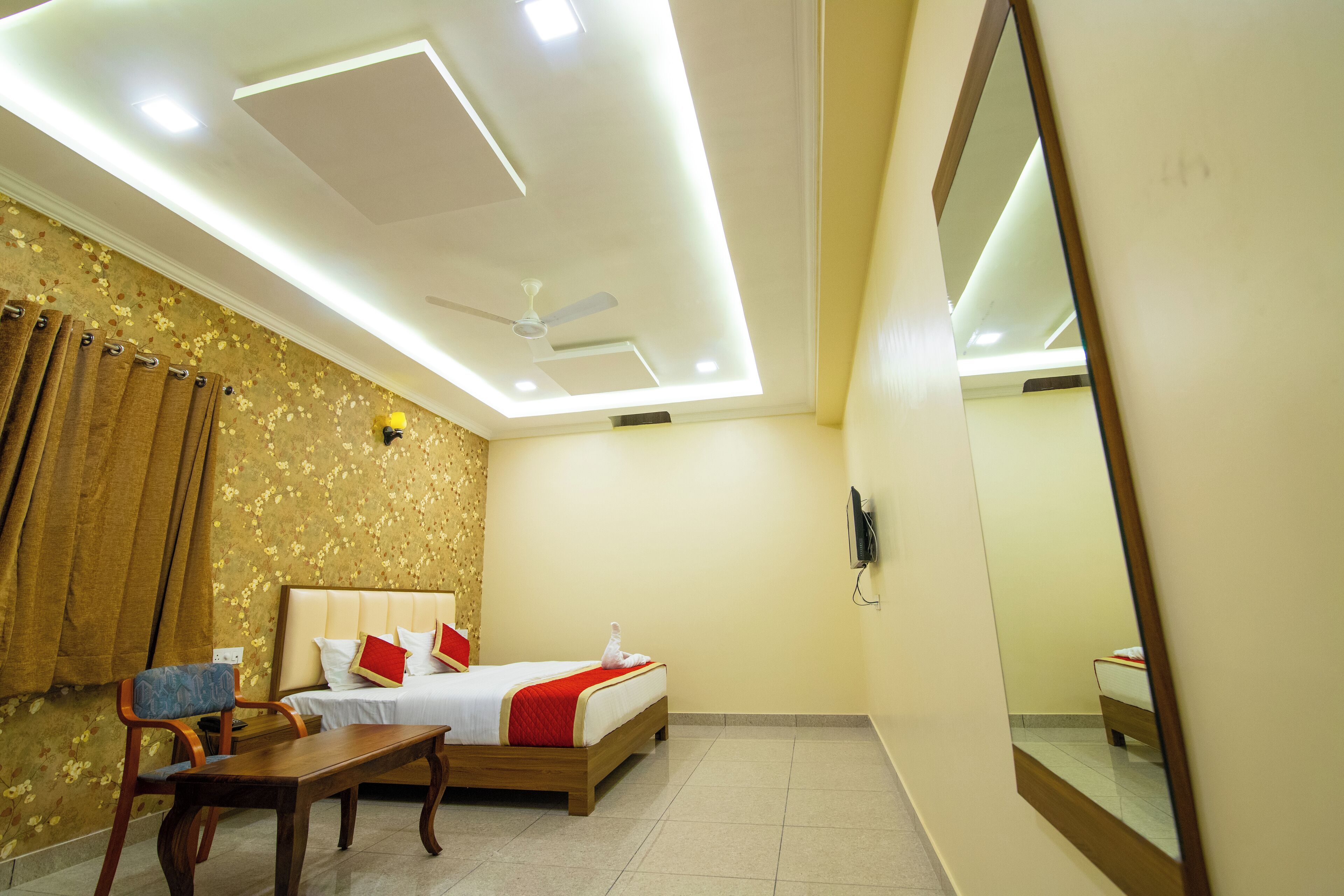 A hotel room with a bed, a desk, a chair, a ceiling fan, and a large mirror.