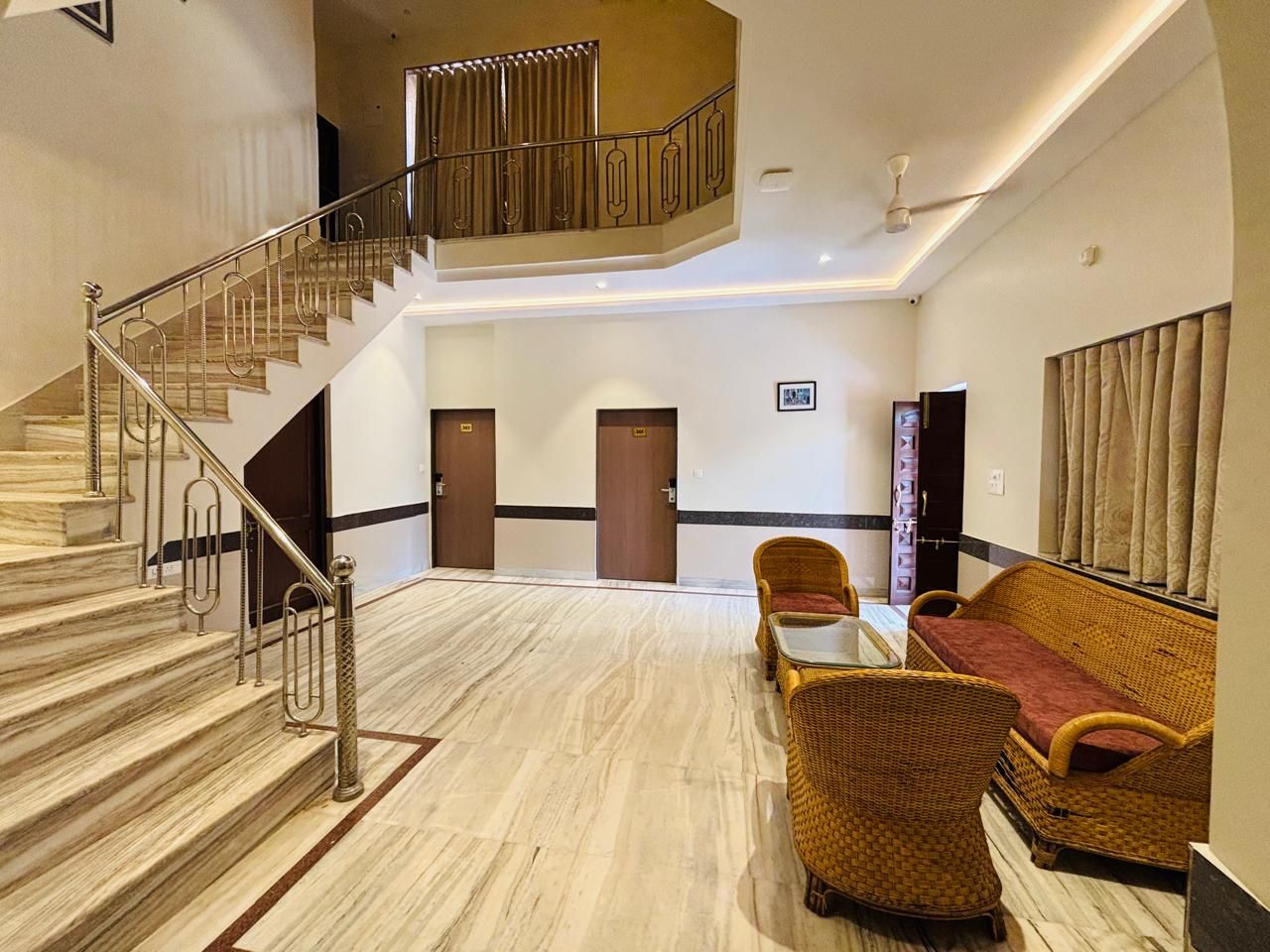 Un vestíbulo de hotel con una escalera de mármol, muebles de mimbre y un ventilador de techo.