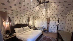 Una tenda-stanza con un letto, un comodino, una lampada e un piccolo tavolo con sedie.