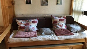 A wooden sofa with patterned cushions and a plain cushion, set against a textured wall with framed artwork. - 1st floor, balcony, tv, 30m², Villard de Lans (Corrençon-en-Vercors)