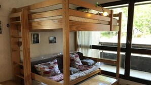 A bunk bed with a wooden frame, a sofa with patterned cushions, and a small wooden table. - 1st floor, balcony, tv, 30m², Villard de Lans (Corrençon-en-Vercors)