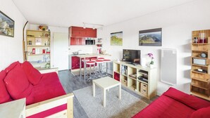 A compact living space with a kitchenette, a dining area, and a seating area with red sofas.