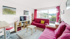 A modern living room with a red sofa, a small table, a TV, and a bookshelf.