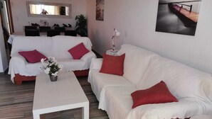 A living room with a white sofa, a white coffee table, and a red cushion. There is a painting on the wall and a plant on the windowsill. - Penthouse first line poniente beach. Elche Park. (Benidorm)