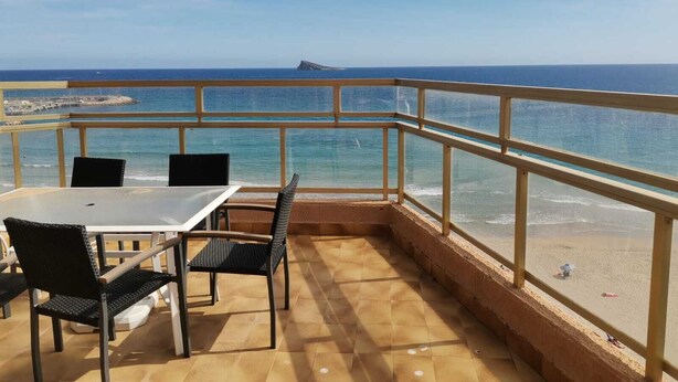 A balcony with a table and chairs overlooking a beach with a clear view of the ocean and a distant island. - Penthouse first line poniente beach. Elche Park. (Benidorm)
