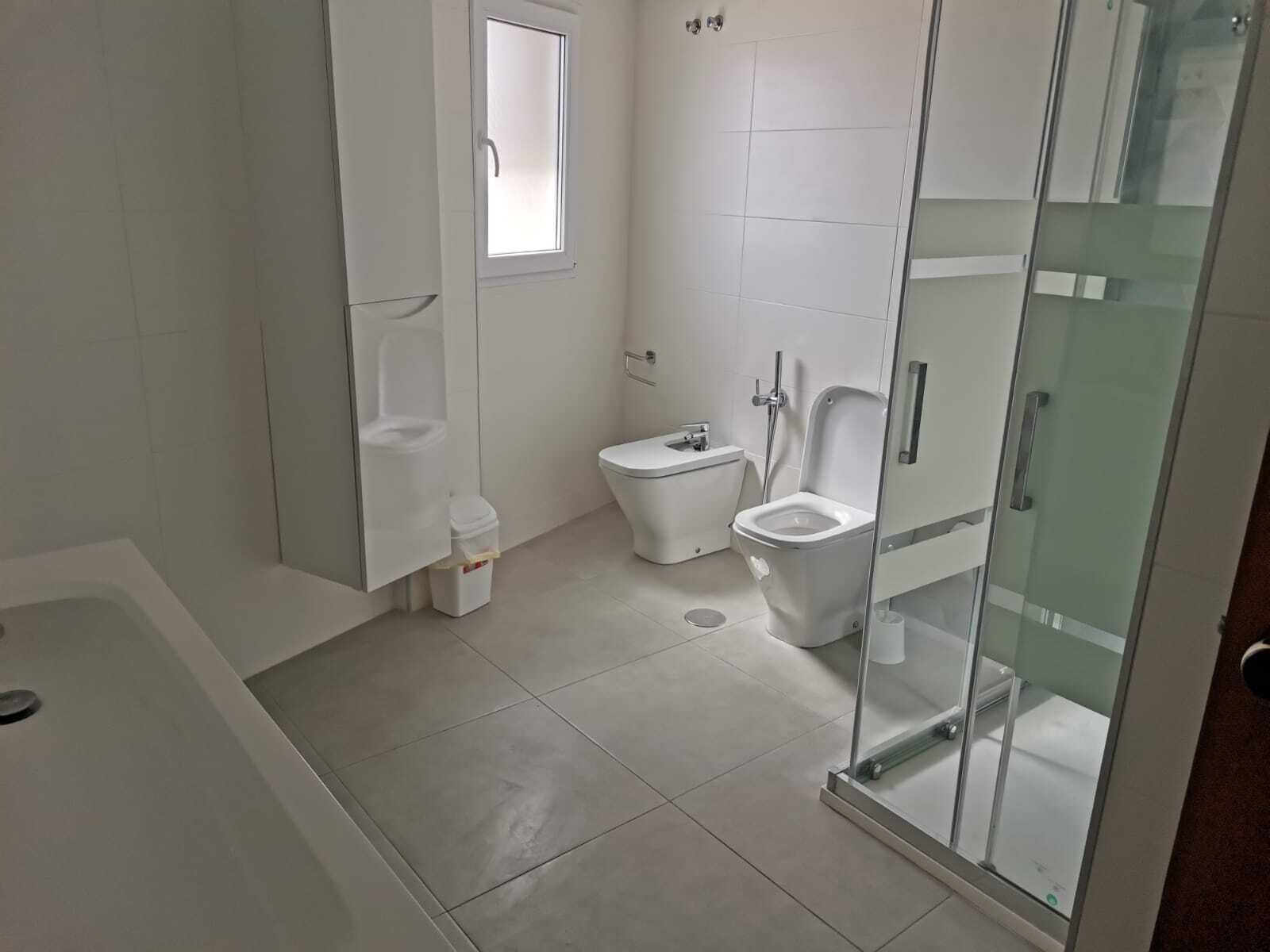 Een moderne badkamer met een douchecabine van glas, een badkuip en twee toiletten.