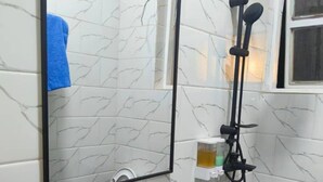 Un baño con baldosas de mármol blanco, un lavamanos blanco, un espejo y un cabezal de ducha de mano.